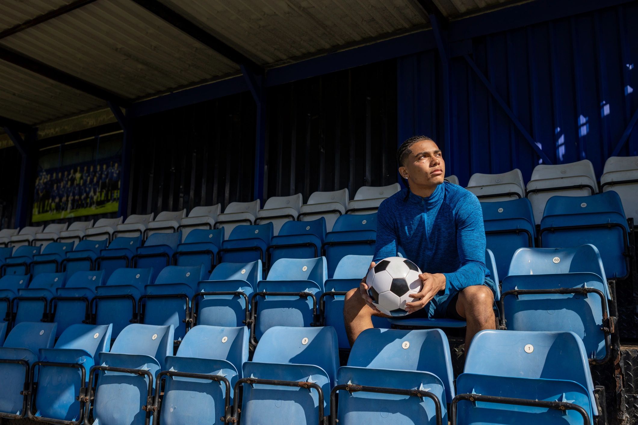 Footballer sitting in the stands with a ball before a match