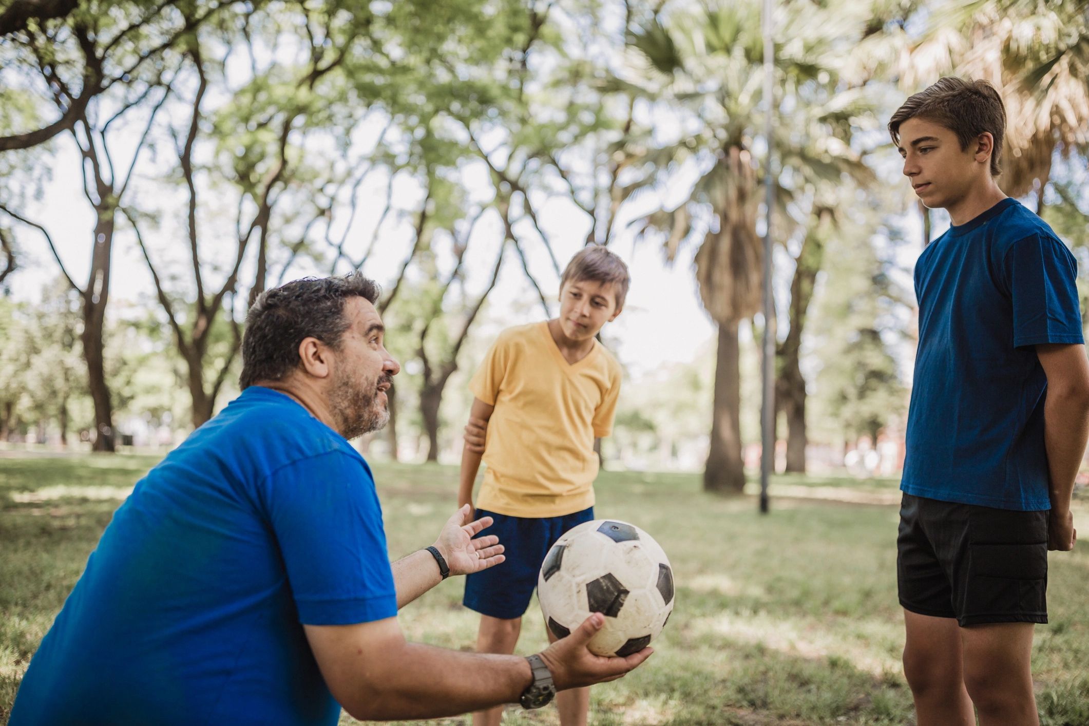 Father teaching children football in a sunny park